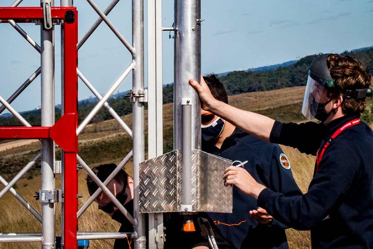Personen monteren een raket op een metalen toren in de buitenlucht.