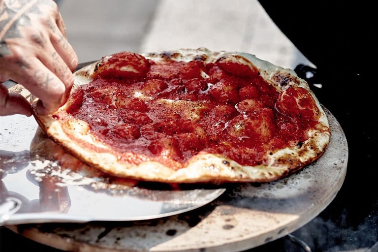 Een pizza met tomatensaus wordt geserveerd op een pizzasteen.