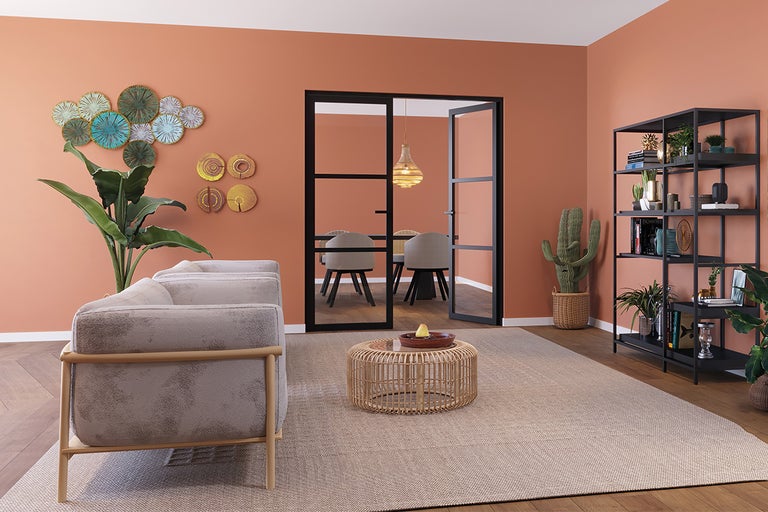 Woonkamer met bank, salontafel van rotan, boekenkast, kamerplanten en schuifdeur