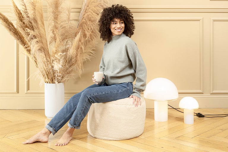 Vrouw zit op een lichte zitzak in een kamer met decoratief gras en lampen