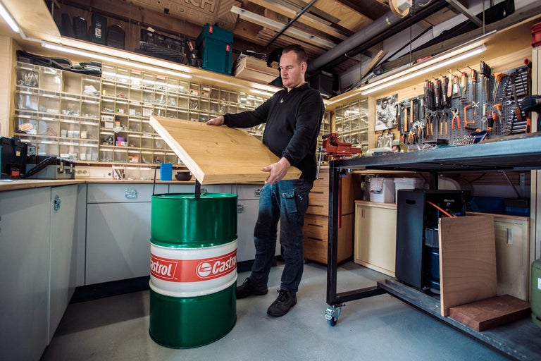 Man in werkplaats tilt houten plaat op olievat met Castrol-logo