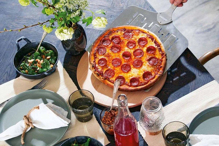 Een gedekte tafel met pizza, salade, drankjes en servies voor een maaltijd