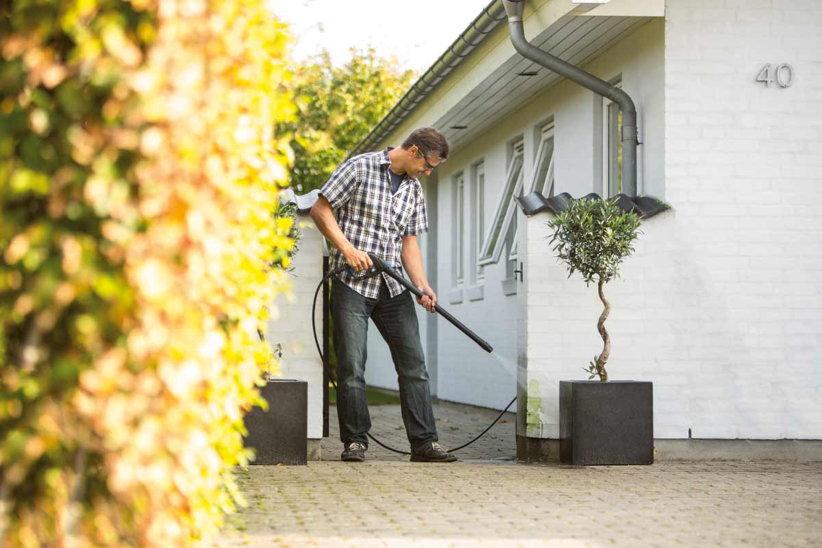 Een man gebruikt een hogedrukreiniger om een huismuur schoon te maken.
