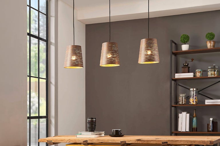 Drie metalen hanglampen hangen boven een houten tafel in een kamer.