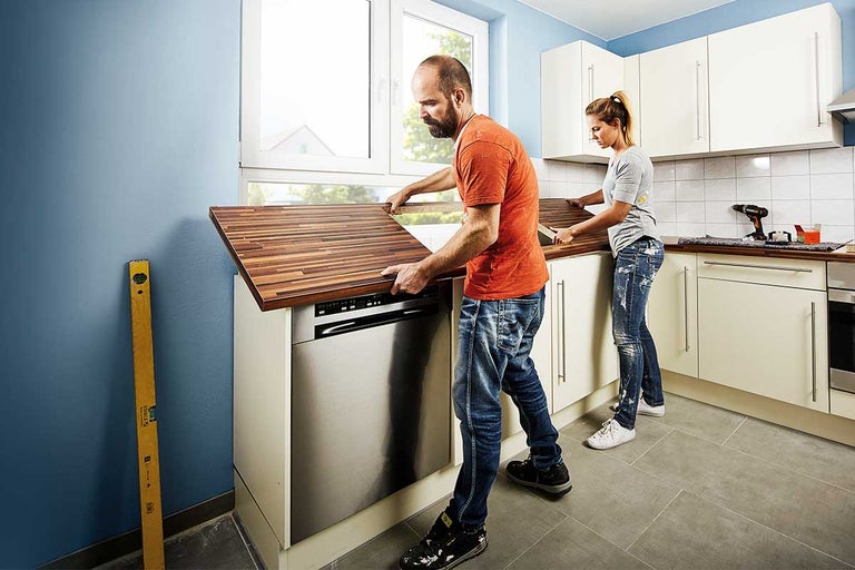 Twee mensen installeren een houten aanrechtblad in een lichte keuken.