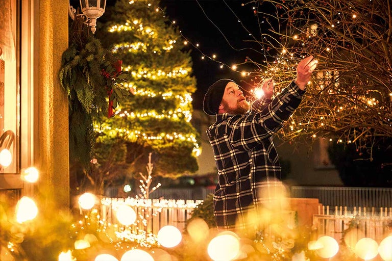 Man versiert een boom met een lichtsnoer buitenshuis. Kerstsfeer met feestelijke verlichting.