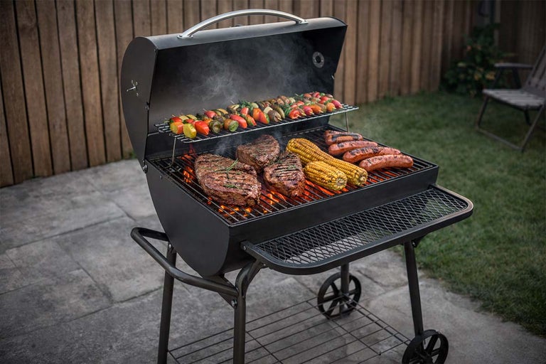 Houtskoolbarbecue met steaks, maïs, worst en groentespiesen op het rooster