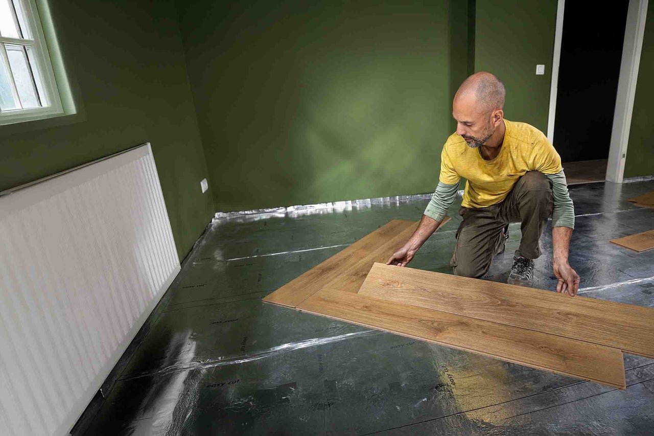 Man legt laminaatvloer op isolerende onderlaag in een kamer.