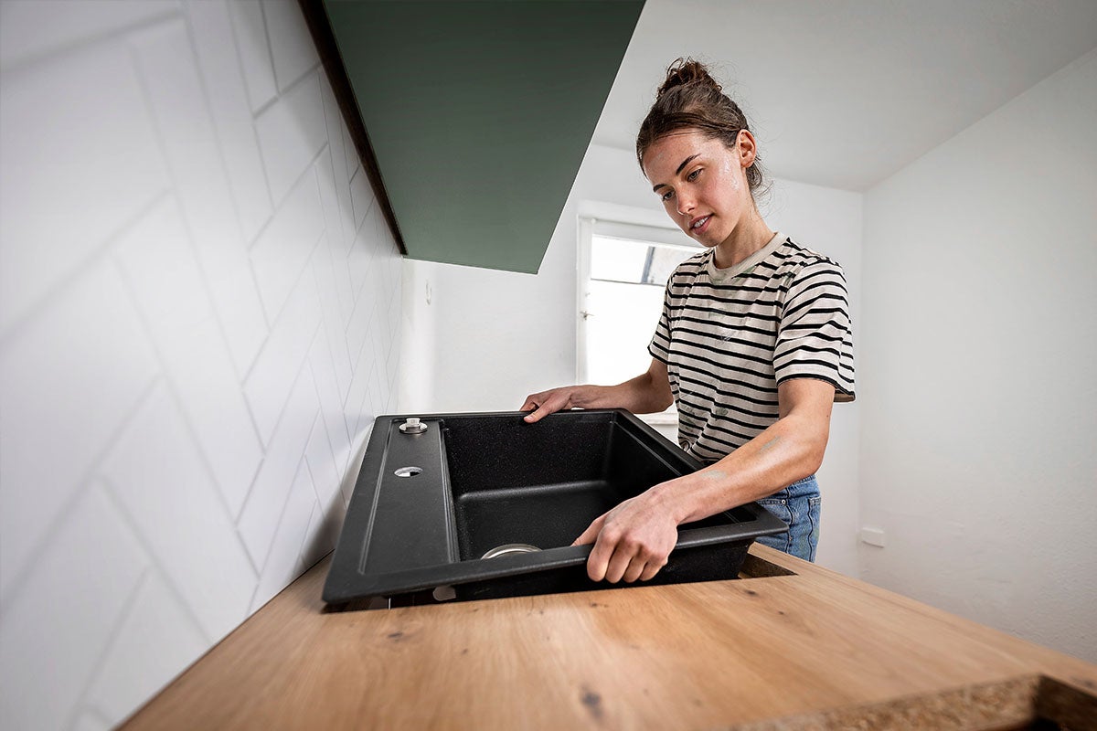 Een vrouw plaatst een spoelbak in de uitsparing van een houten keukenwerkblad.