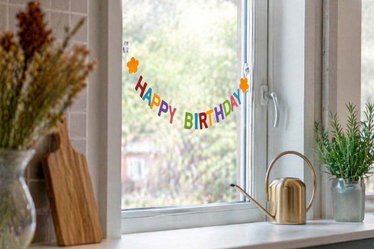 Raamsticker Happy Birthday met gekleurde letters en bloemen op een glazen ruit in een lichte keuken.
