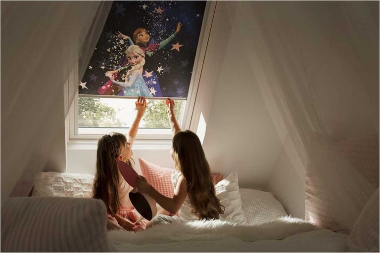 Twee kinderen in bed kijken naar een dakraam rolgordijn met een motief uit de film Frozen.