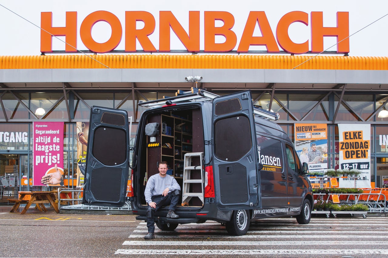 Een vakman zit voor een bestelwagen voor een Hornbach bouwmarkt.