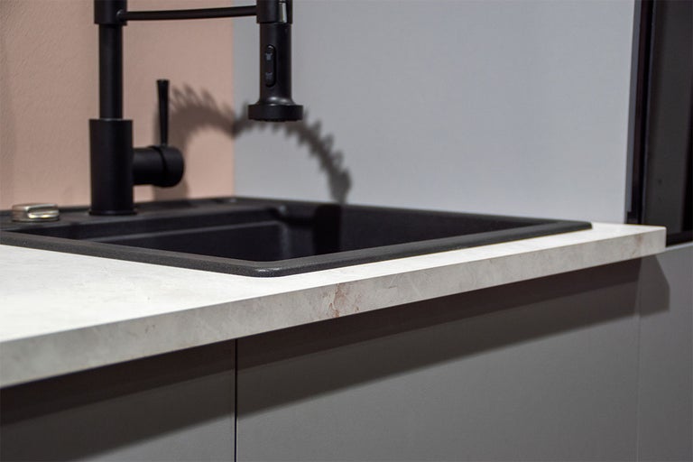 Inbouwspoelbak van donker composietmateriaal met matzwarte keukenkraan op een licht aanrechtblad met steeneffect.
