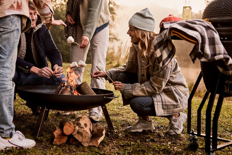 Groep mensen roostert marshmallows boven een vuurschaal in de buitenlucht.