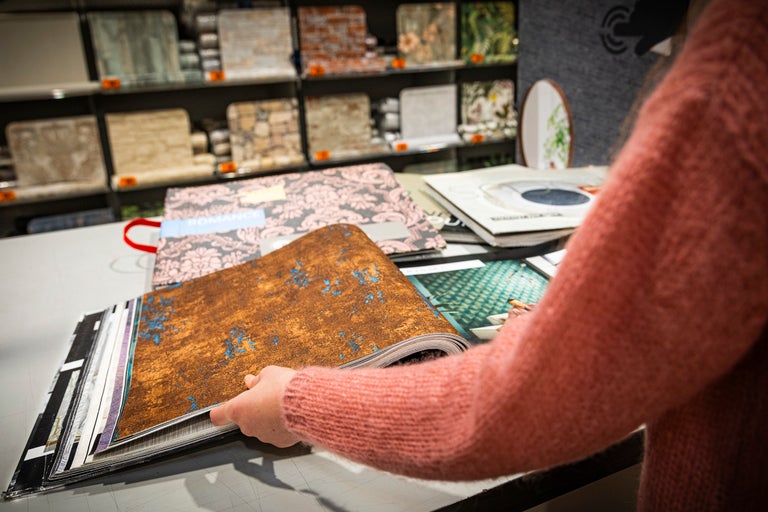 Een persoon bladert door een behangstalenboek in de Hornbach webshop.