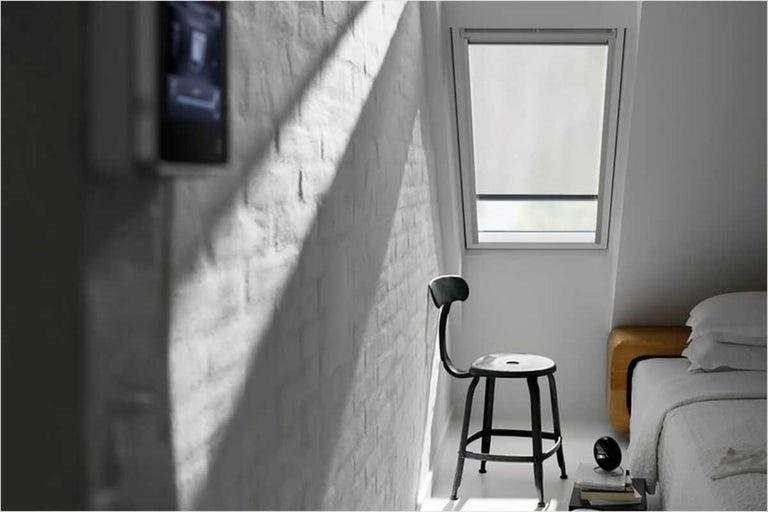 Lichte slaapkamer met dakraam en rolgordijn, stoel en bakstenen muur