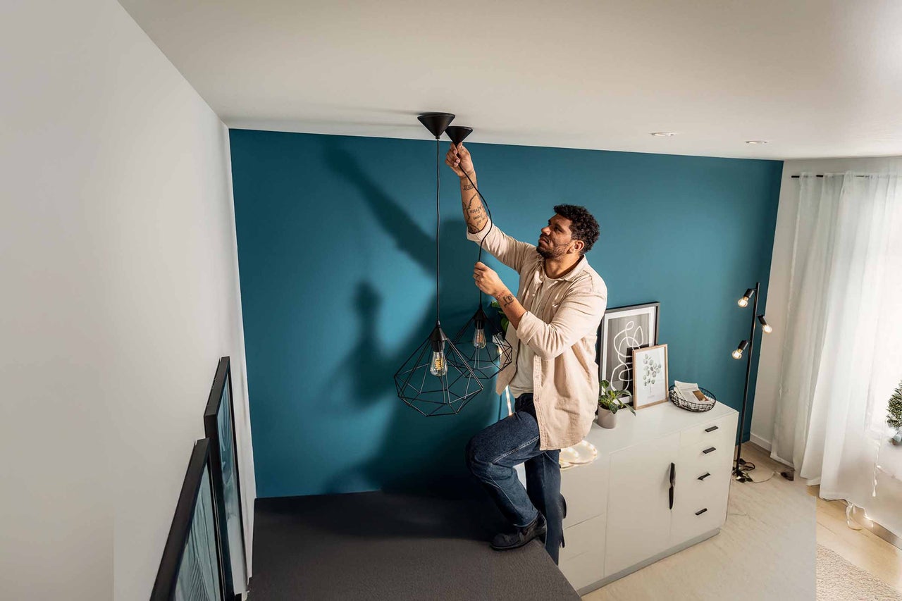 Man installeert hanglampen met een geometrische lampenkap in een heldere kamer.