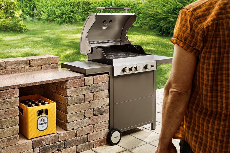 Gasbarbecue met open deksel en krat met drankjes in de tuin