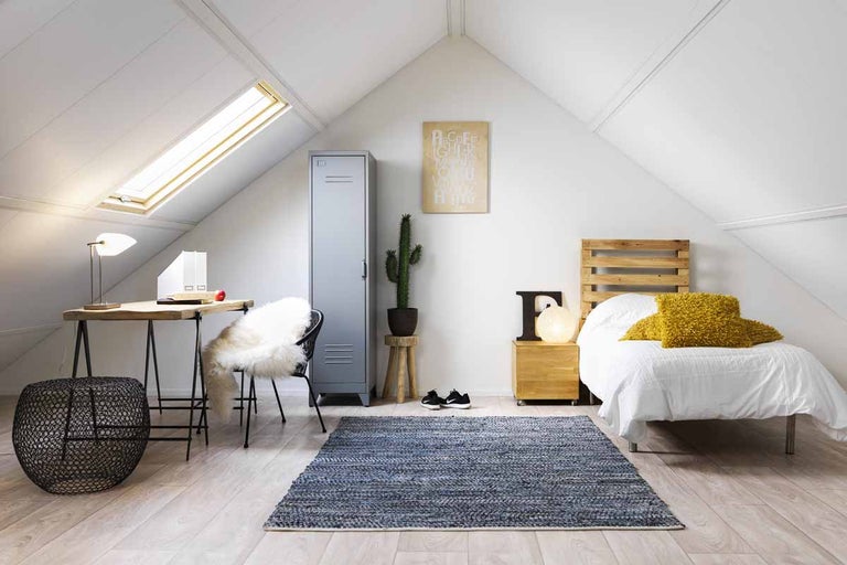 Lichte zolderkamer met bureau, bed en blauw vloerkleed