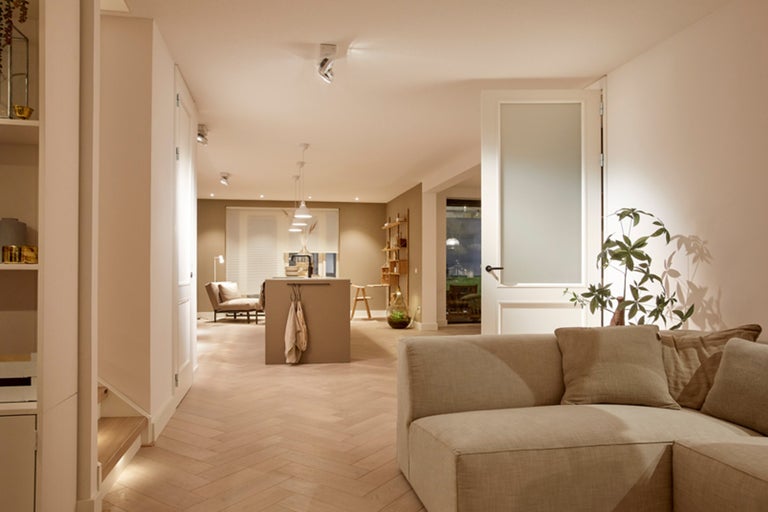 Lichte woonkamer met bank, open keuken en houten vloer in visgraatmotief.