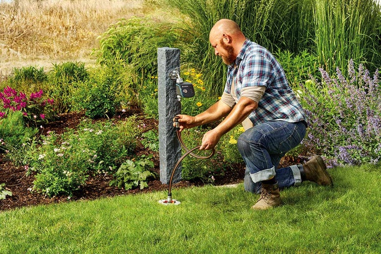 Man sluit een tuinslang aan op een kraan in de tuin