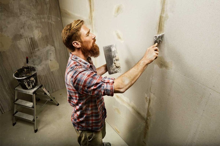 Man pleistert muur in kamer met plamuurmes en vulmiddel