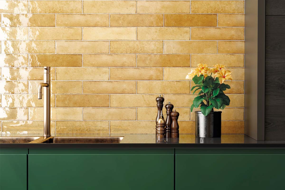 Keukenscène met gele wandtegels in horizontale band, kraan, gootsteen, kruidenpot en kruidenmolens op een groen keukenblok