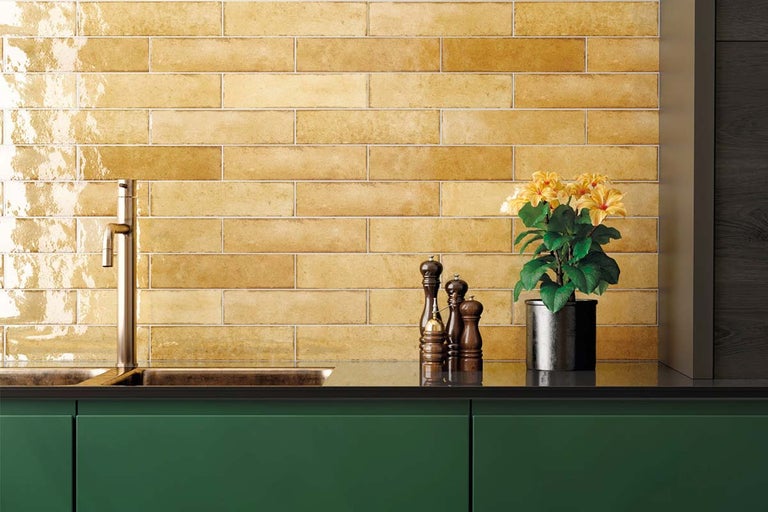 Keukenscène met gele wandtegels in horizontale band, kraan, gootsteen, kruidenpot en kruidenmolens op een groen keukenblok
