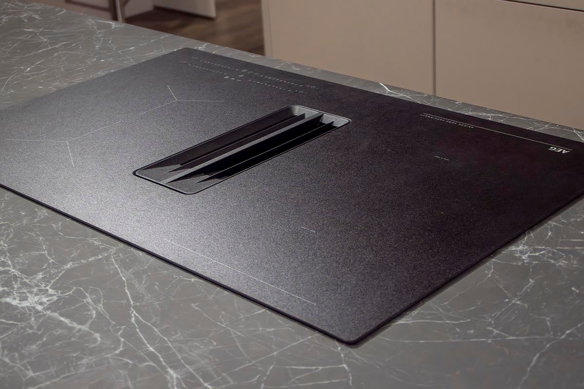 Zwarte AEG inductiekookplaat met geïntegreerde afzuigkap op een keukenblad.