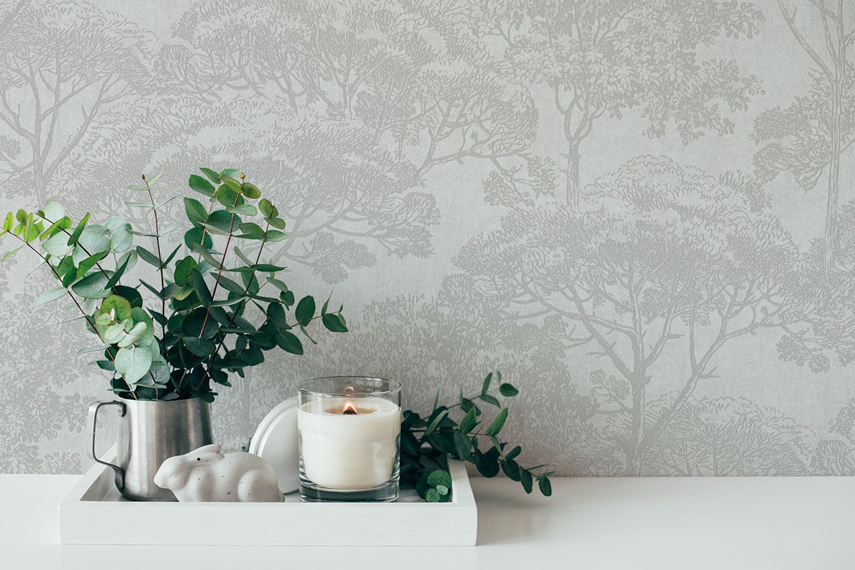 Behang met bomenmotief achter decoratie van eucalyptusstelen, een kaars en een haasfiguur op een dienblad.