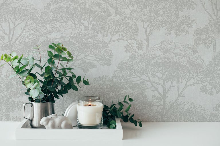 Behang met bomenmotief achter decoratie van eucalyptusstelen, een kaars en een haasfiguur op een dienblad.