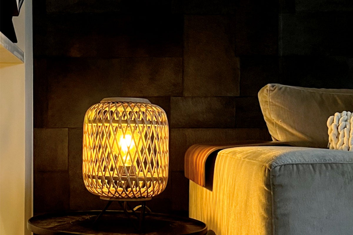 Tafellamp met gevlochten rotan design op een salontafel naast een bank in een gezellige woonkamer.