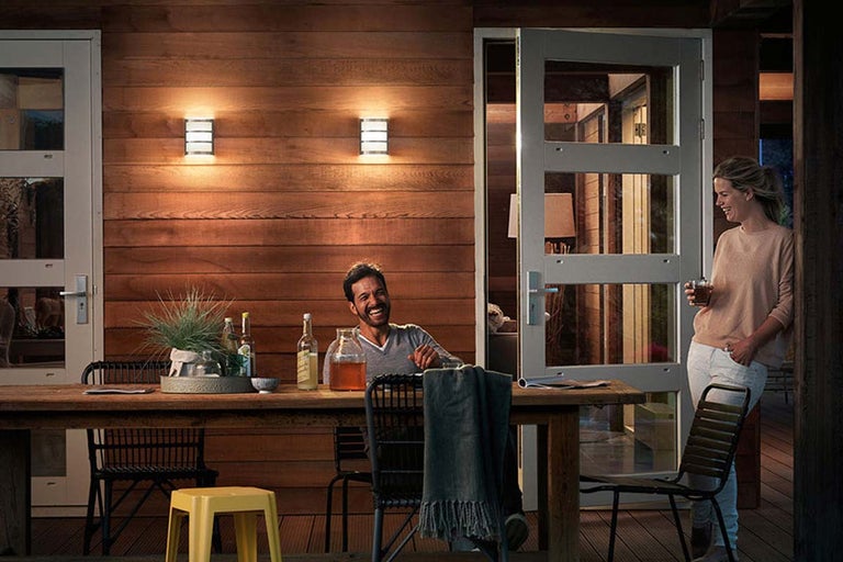 Uitnodigend terras met houten bekleding, verlichte wandlampen en gezellige tafelsetting