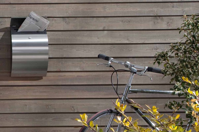 Roestvrijstalen brievenbus met krant op houten gevel en fiets