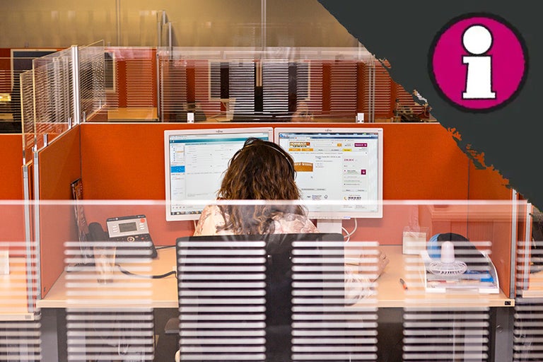 Klantenservice medewerker aan een bureau met computers en headset achter een scheidingswand