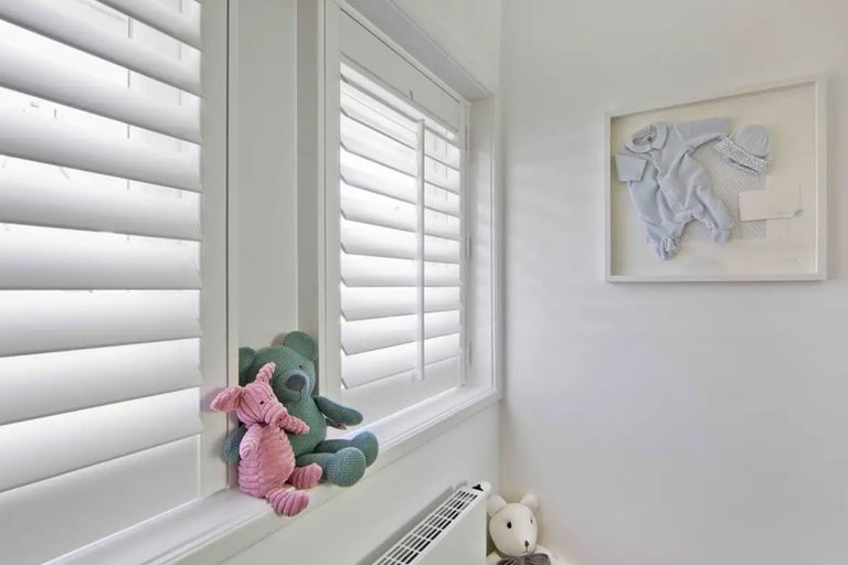 Lichte kamer met jaloezieën, teddyberen en ingelijste babykleding