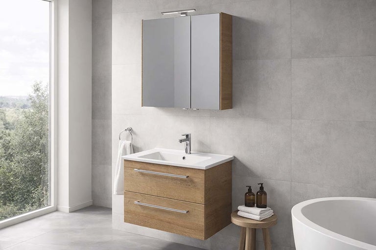 Moderne, lichte badkamer met wastafelonderkast in houtlook, witte wastafel, chromen kraan en spiegelkast tegen een grijze tegelwand.