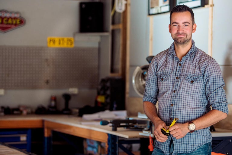 Een man staat in een werkplaats met gereedschap en apparatuur op de achtergrond.