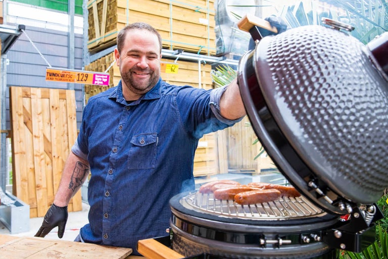 Man grilt worstjes op een keramische grill in de buitenlucht
