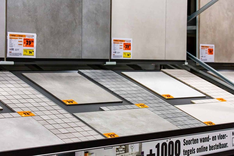 Tegels in verschillende ontwerpen en prijsklassen in een bouwmarkt schap.