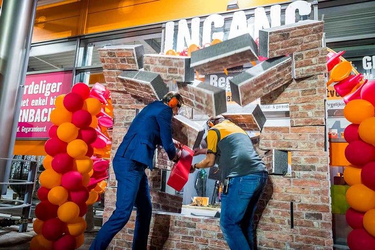 Twee mensen vernielen een bakstenen muur voor de ingang van een Hornbach bouwmarkt.