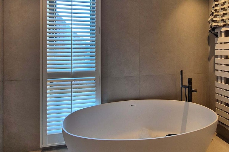 Moderne badkamer met vrijstaand bad, lamellenraam en wandtegels in een minimalistische stijl.