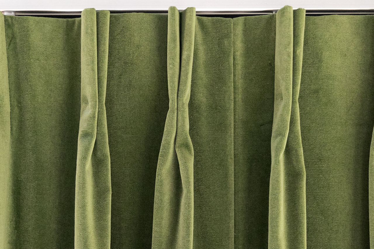 Fluwelen gordijn in groen met plooiband, opgehangen aan een gordijnrail.