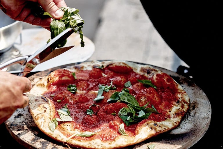 Pizza met tomaten en basilicum wordt gegarneerd met een schaar.