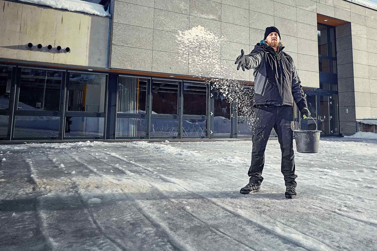 Een persoon strooit strooizout om ijs te bestrijden voor een gebouw.