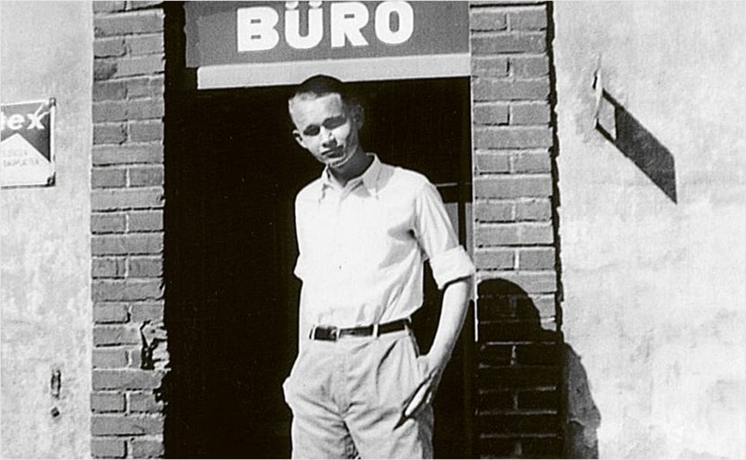 Een jonge man staat voor een kantoorgebouw.