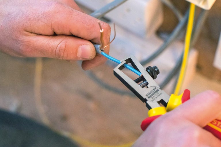 Elektricien die met een draadstriptang een kabel stript.