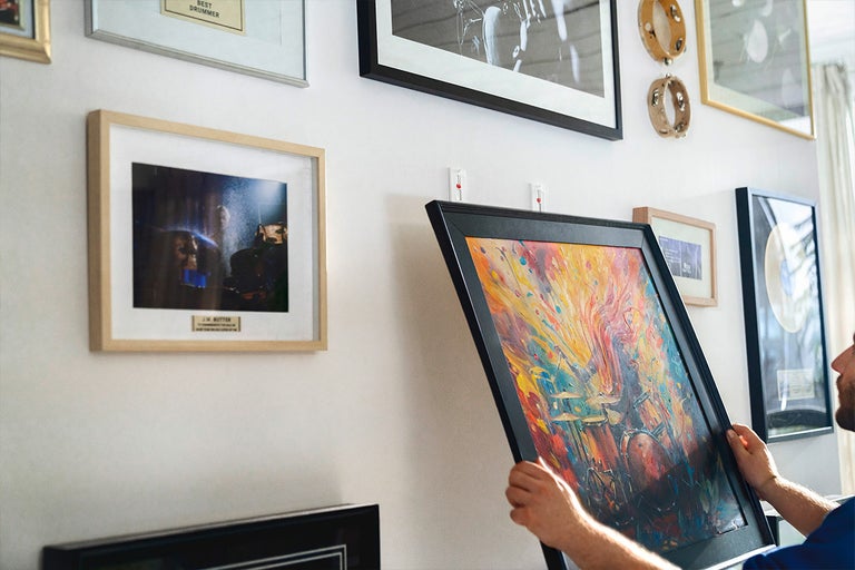 Persoon hangt ingelijst kunstwerk op met plakstrips aan de muur om een galerij te creëren.