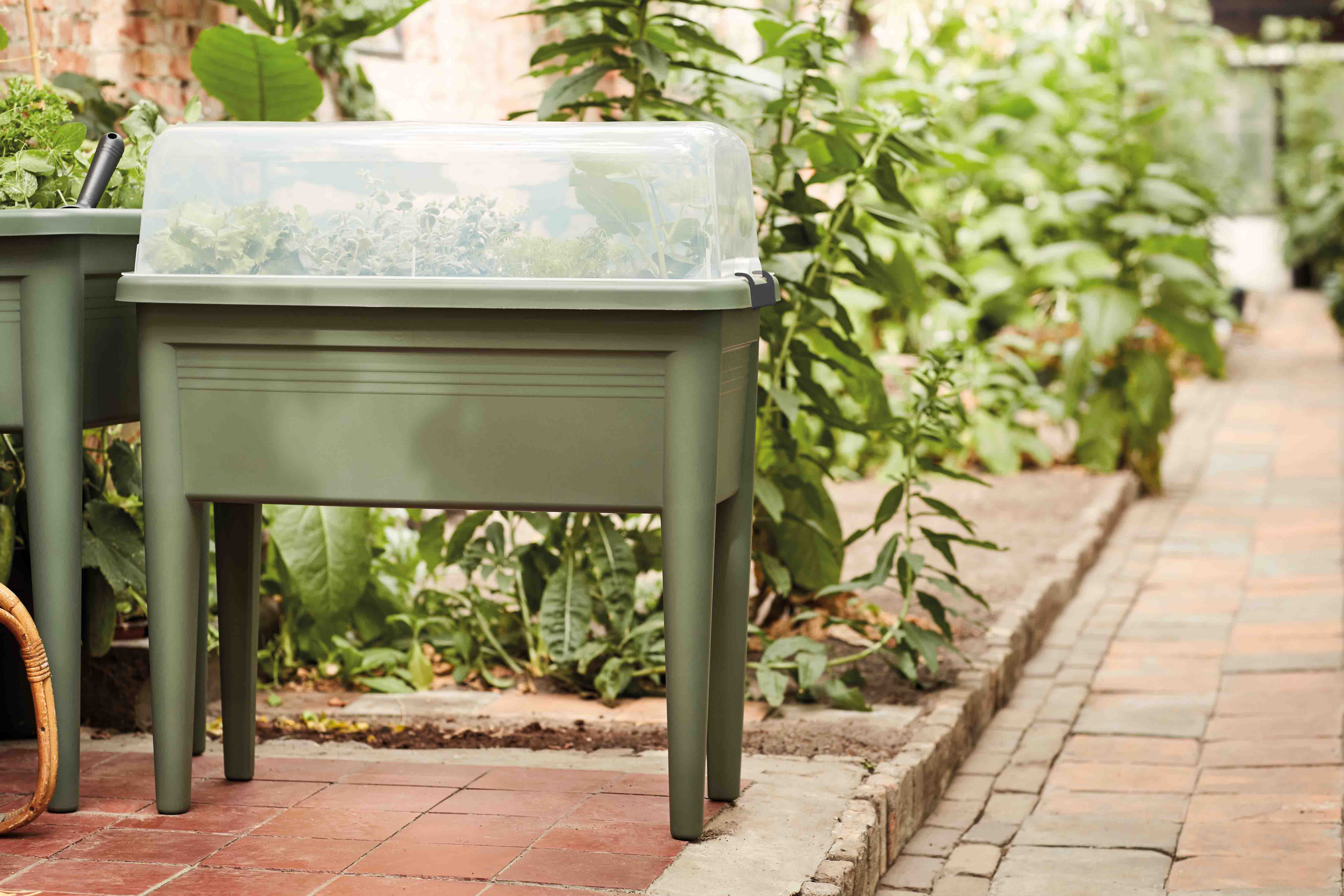 Kunststof plantenbak op poten met transparante afdekking in de tuin