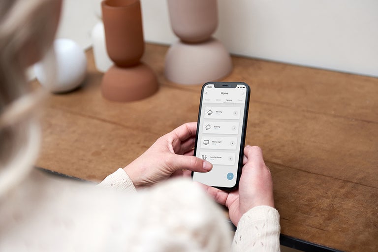 Een persoon bedient een smartphone met een smart home app op een houten tafel.